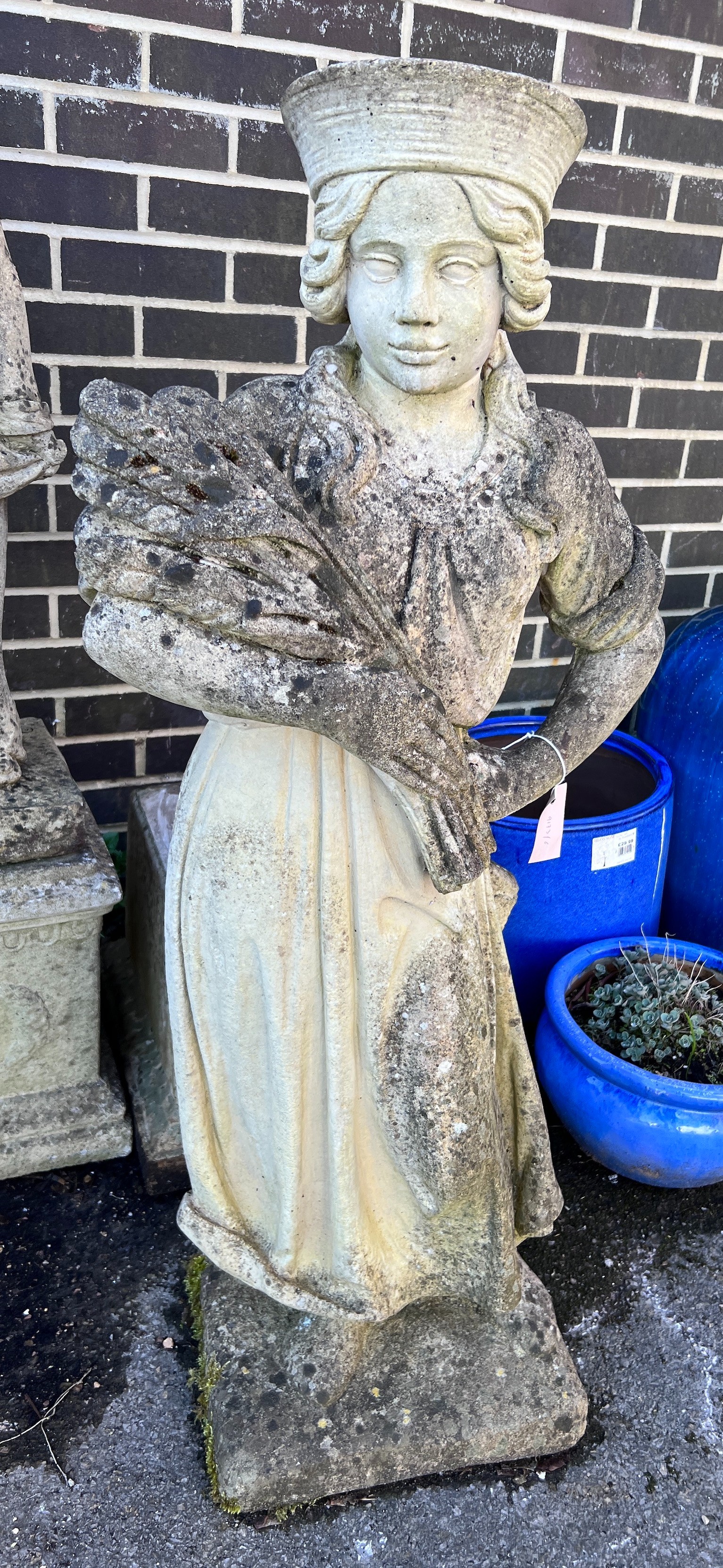 A reconstituted stone garden ornament of a female figure with a sheaf of corn on square plinth base, height approx. 156cm *Please note the sale commences at 9am.